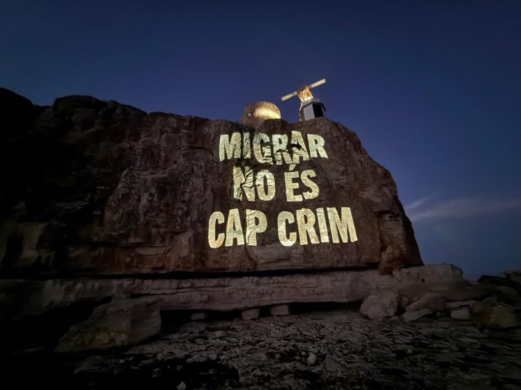 Proyección del Grupo de Acción Antifronteras Laissez Passer, en el marco de una campaña que, en verano de 2025, proyectó en la Torre de en Beu -donde se encuentra el IVE, el radar del sistema de vigilancia de embarcaciones marítimas-, da la bienvenida a las personas migrantes en 22 idiomas. | Fotografía de Laissez Passer